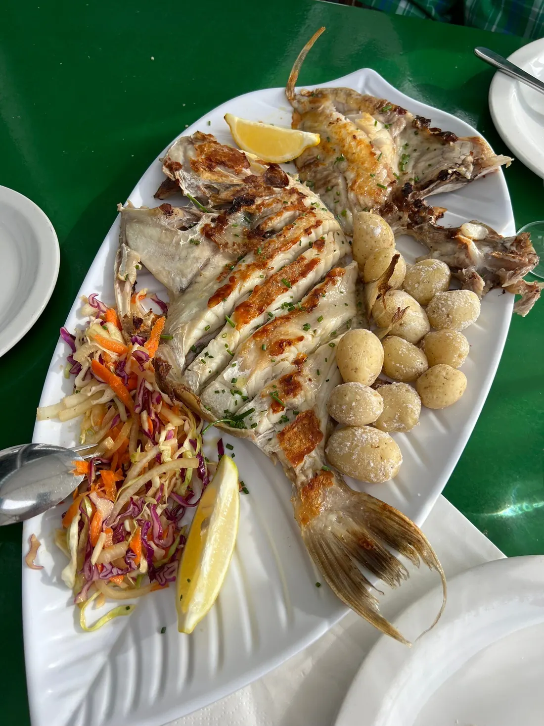 Pescado abierto a la plancha con papas arrugadas, ensalada y limón en una fuente con forma de pez