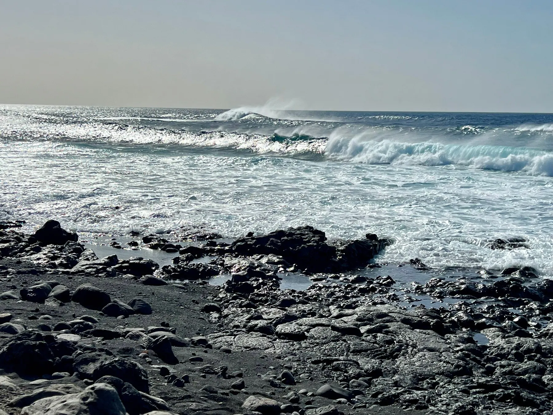 Olas rompiendo junto a las rocas de lava y los charcos de marea frente al restaurante